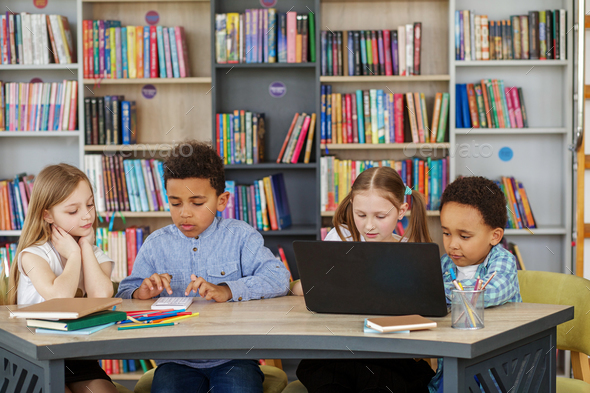 Multiracial group of children sitting in row at school classroom and using laptops. Back to school